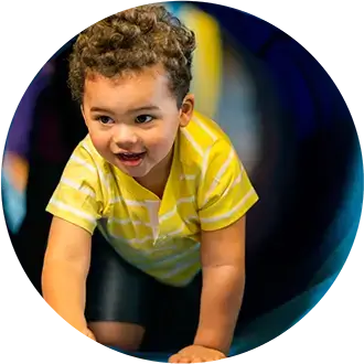 A young child in a yellow striped shirt crawling through a tunnel.
