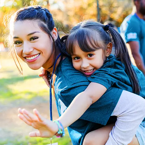 A smiling young woman giving a piggyback ride to a young girl.