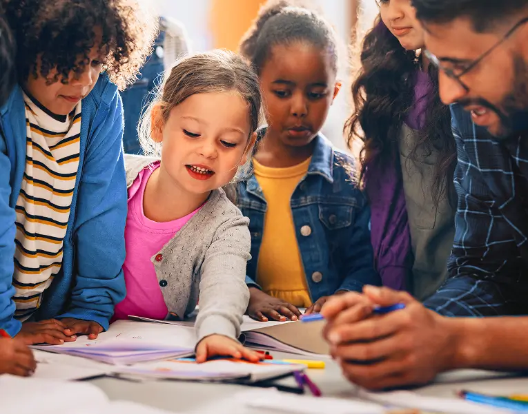 A teacher and four children gathered around a table, working on a drawing project together.